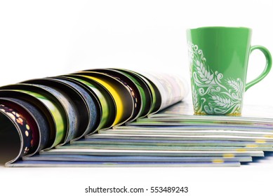 Stack of magazines with cup of coffee on top.