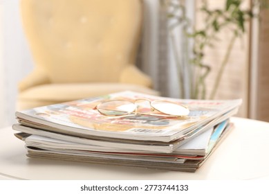 Stack of magazines and glasses on white table indoors, closeup. Space for text
