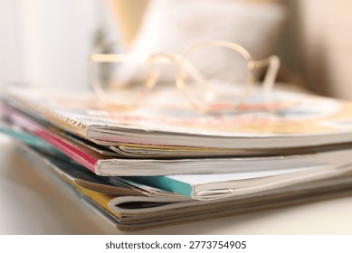 Stack of magazines and glasses on white table indoors, closeup