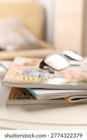 Stack of magazines and glasses on white table indoors, closeup. Space for text