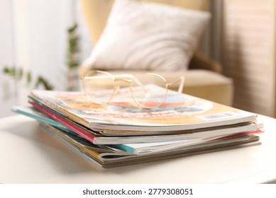 Stack of magazines and glasses on white table indoors, closeup. Space for text