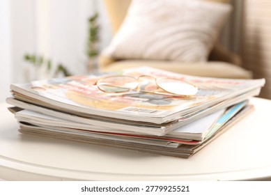 Stack of magazines and glasses on white table indoors, closeup. Space for text