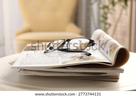 Stack of magazines and glasses on white table indoors, closeup. Space for text