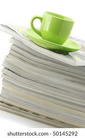 Stack of magazines and green cup of coffee on white background.