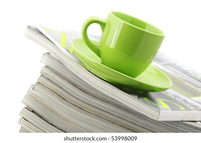 Stack of magazines and green cup of coffee on white background.