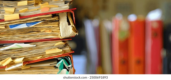 stack of messy file folders with narrow depth of field, blurred office  in the back,red tape, bureaucracy,aministration,business concept. 