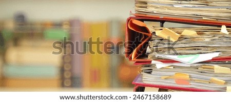stack of messy file folders with narrow depth of field, blurred bookshelf  in the back,red tape, bureaucracy,aministration,business concept. 
