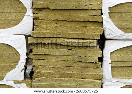 Stack of mineral wool insulation boards in torn plastic wrap shows textured surface of construction material up close.