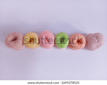 A stack of mini donuts (or coconut candy) and round sweets in pastel colors (pink, yellow, green, orange). A typical Indonesian market snack.