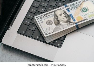 A stack of money on a laptop computer keyboard. Concept of financial savings, banking services, making money online and deposit.
