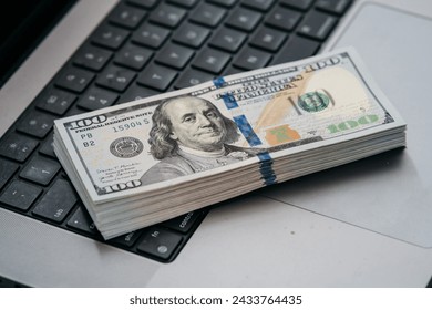 A stack of money on a laptop computer keyboard. Concept of financial savings, banking services, making money online and deposit.