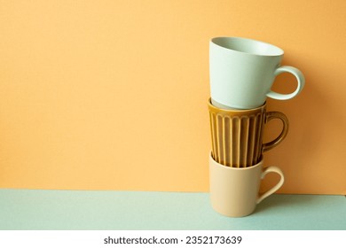 Stack of mug cup on mint green table. orange wall background. copy space
