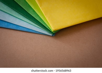 a stack of multi colored tissue paper spread out in a fan on a background of brown cardboard, with a vignette