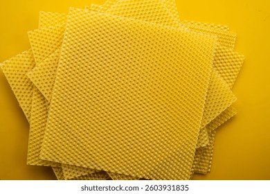 Stack of Natural beeswax sheets on yellow background, flat lay. Close-up