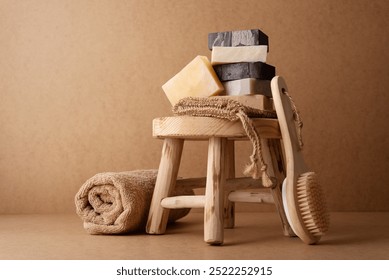 A stack of natural handmade soap bars with a wooden back brush and rolled towel on a rustic wooden stool. Perfect for spa, skincare, or eco-friendly self-care concepts in minimalist settings.