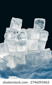 A stack of natural shiny ice cubes in the snow on a black background.