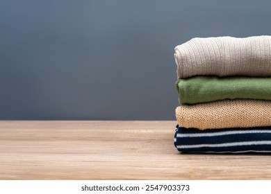 A stack of neatly folded clothes on a wooden table against a gray background. Copy space for text. - Powered by Shutterstock