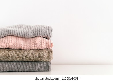Stack of neatly folded knitwear. Minimal lifestyle, capsule wardrobe. Detail of cozy winter interior