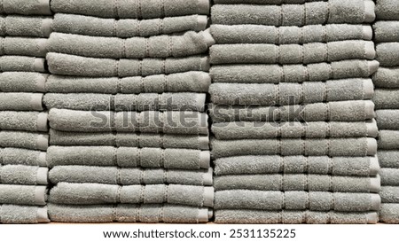 A stack of neatly folded, same-colored towels sits on a shelf in a home decor store. The towels create a clean, organized, and textured display.