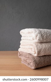 Stack of neutral colored cotton bath towels on wooden table. Concept of cleanliness, cleaning, laundry and hygiene. Towels made of organic natural fabric, space for text