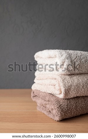 Stack of neutral colored cotton bath towels on wooden table. Concept of cleanliness, cleaning, laundry and hygiene. Towels made of organic natural fabric, space for text