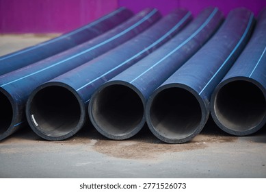 Stack of new black HDPE plastic pipes with blue stripes for cold water supply. Industrial construction site and municipal infrastructure background