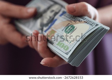 A stack of new one-hundred dollar bills being held in a pair of hands.