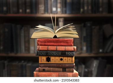 A stack of new study books on the table against the background of a bookshelf in library. - Shutterstock ID 2193543383