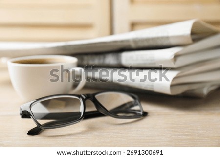 Stack of newspapers, coffee and glasses on wooden table, closeup