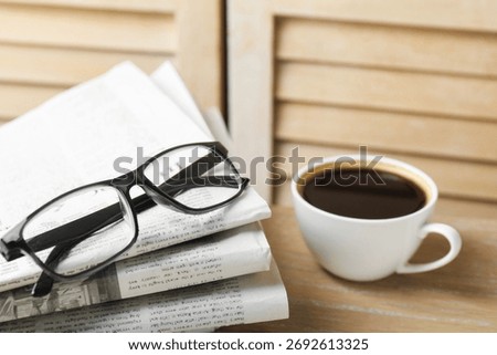 Stack of newspapers, coffee and glasses on wooden table, closeup