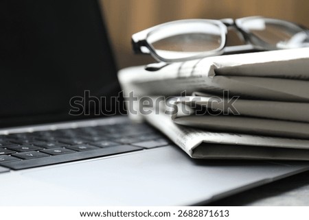 Stack of newspapers, laptop and glasses on table, closeup