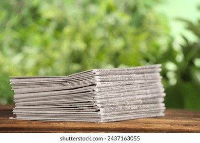 Stack of newspapers on wooden table against blurred green background. Journalist's work