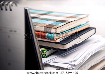 A stack of notebooks, documents, and a calendar on the desk