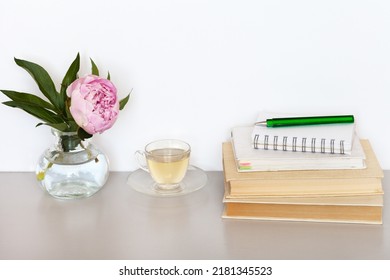 A Stack Of Old Books With Bookmarks, A Notepad With A Pen For Notes, Evening Herbal Tea In A Glass Cup And A Pink Peony Flower On A Light Table. Home Comfort, Spring Still Life