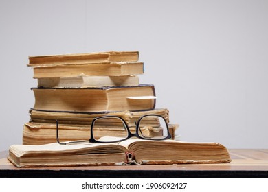 A Stack Of Old Books With Bookmarks On A Wooden Table On A Gray Background. Glasses Lie On An Open Book.