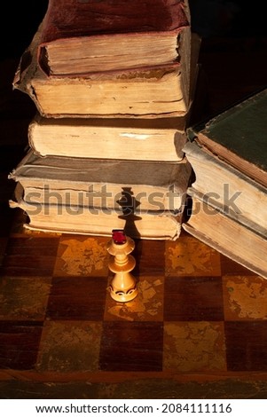 Stack of old books on a chessboard and king figure with shadow on the books