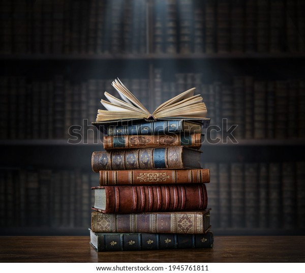 A stack of old books on table against background\
of bookshelf in library. Ancient books as a symbol of knowledge,\
history, memory and information. Conceptual background on\
education, literature topics