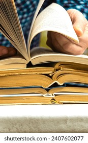 A stack of old books open and a hand flipping through the pages. The concept of careful reading.