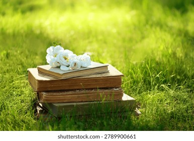 Stack of old books and white wild rose flowers in green garden, sunny nature background. love of reading, relax vacation concept. inspiration atmosphere romantic image. Beautiful landscape with books