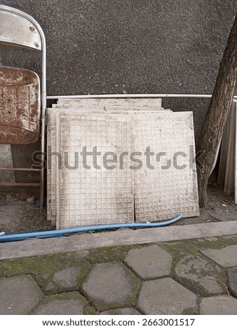 Stack of old dirty tiles on roadside beside metal chair and tree, showing abandoned building material.