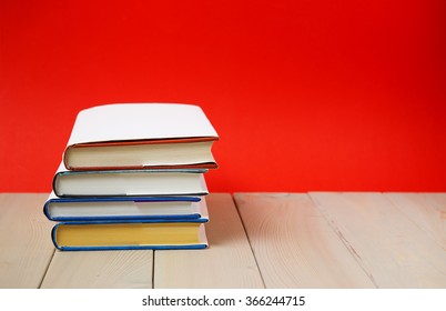 Stack of old hardback books, diary, on wooden deck table and red background.