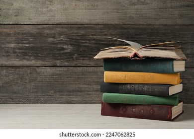 Stack of old hardcover books on white wooden table, space for text