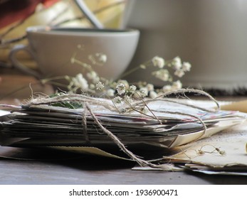 A stack of old letters and papers tied with twine on a wooden table.  In the background a cup and white dried flowers.  Vintage