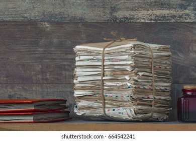 A stack of old letters and two red photo albums lie on the table