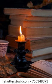 stack of old tattered book on a wooden table lighted candle and glasses