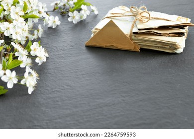 Stack of old torn vintage letters on yellowed paper against black granite table with cherry blossom branch.Retro concept top view with copy space. Vintage  concept flat lay top view with copy space.