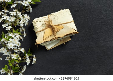 Stack of old torn vintage letters on yellowed paper against black granite table with cherry blossom branch.Retro concept top view with copy space. Vintage  concept flat lay top view with copy space.