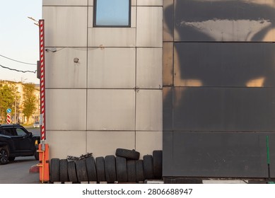 Stack of old used car tires leaning against a modern building wall next to a parking barrier