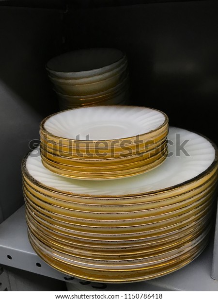 Stack of old used vintage colorful\
dinner plates dishes for sale on shelf in thrift shop\
store