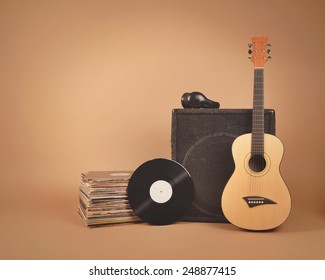 A Stack Of Old Vinyl Records And Acoustic Wooden Guitar With An Amplifier Are Isolated On A Brown Background For A Music Or Band Concept.